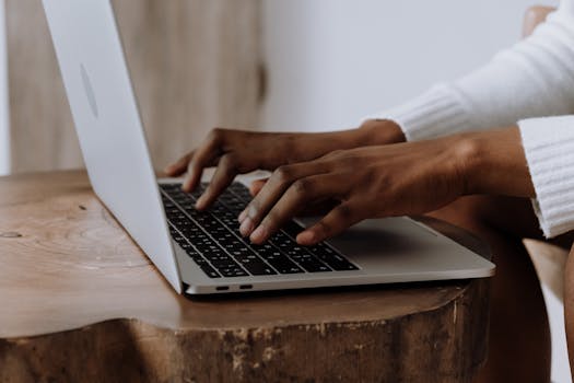Hands typing on a laptop in a cozy indoor setting, focusing on technology and digital work.